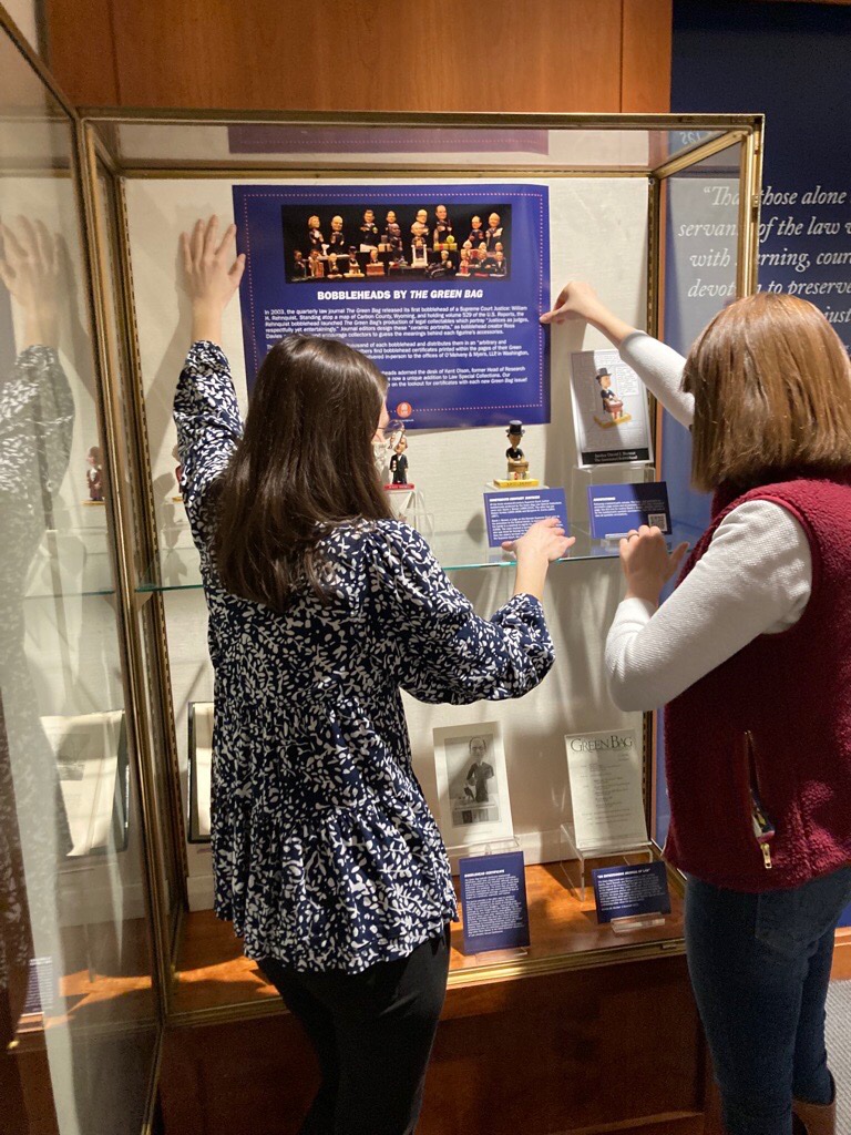 Color photograph of two women placing bobblehead figurines in exhibit cases"